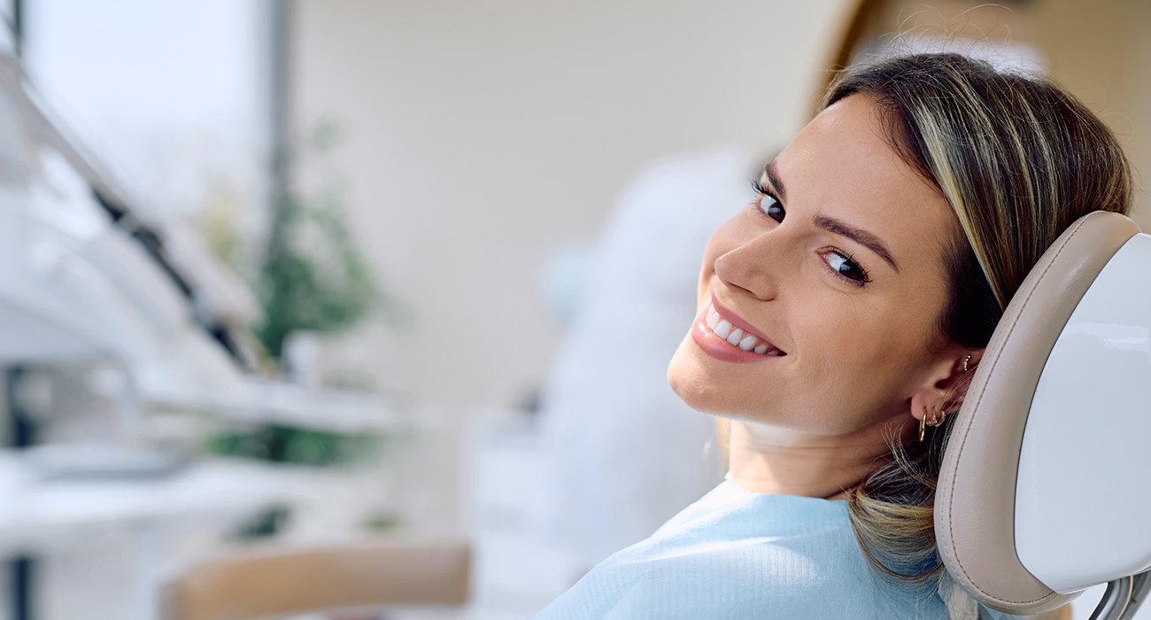 Woman smiling and looking at camera from dental chair, wearing protective bib during dental examination for oral hygiene