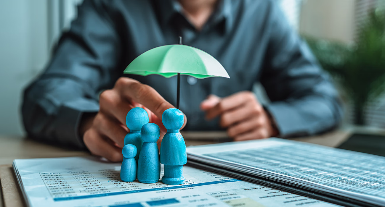 A wooden doll under an umbrella holding by agent represent insurance